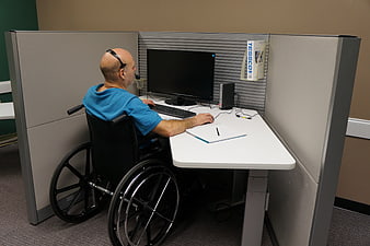 Man in wheelchair working on computer in office cubicle