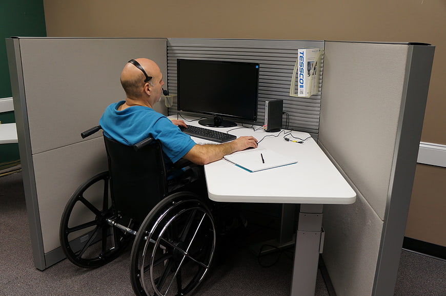 Man in wheelchair working on computer in office cubicle