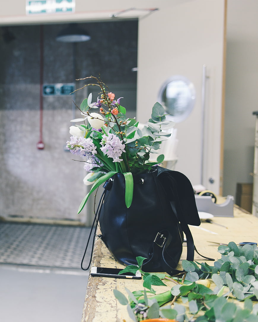 Floral arrangement in black leather bag on wooden table