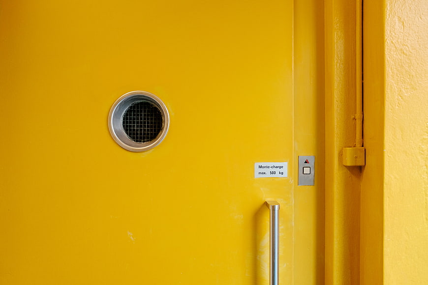 Close-up of a yellow freight elevator door with handle and call button