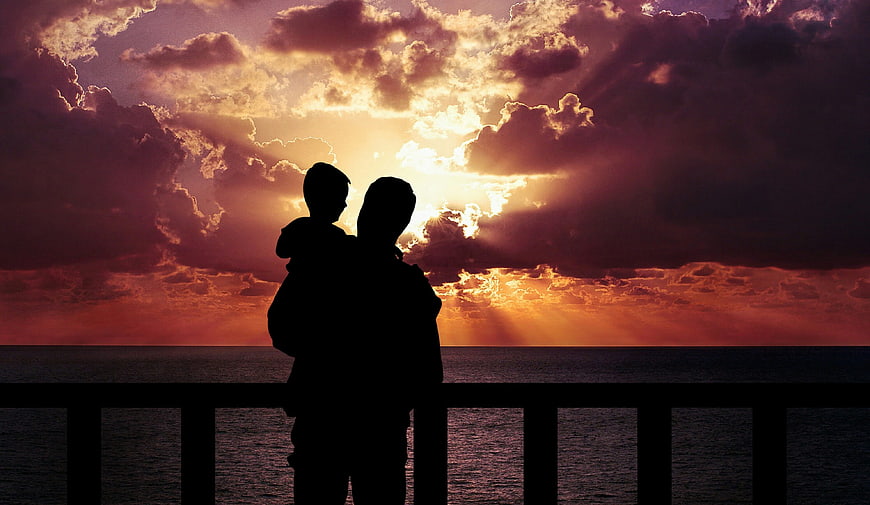 Silhouette of Father and Son Watching Sunset Over Ocean
