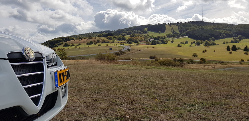 White Alfa Romeo car parked in green countryside landscape