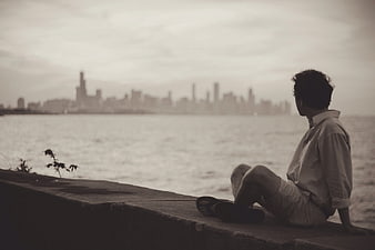 Man sitting by waterfront looking at city skyline