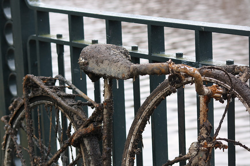 Muddy rusty bicycle leaning against green railing by canal