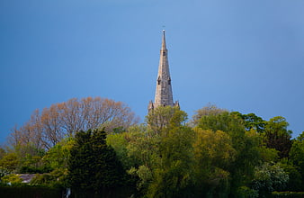 Stone church spire rising above lush green trees against blue sky