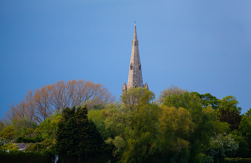 Stone church spire rising above lush green trees against blue sky