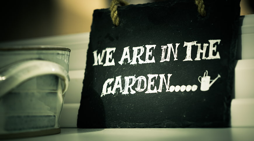 Chalkboard sign reading 'We are in the garden' with watering can