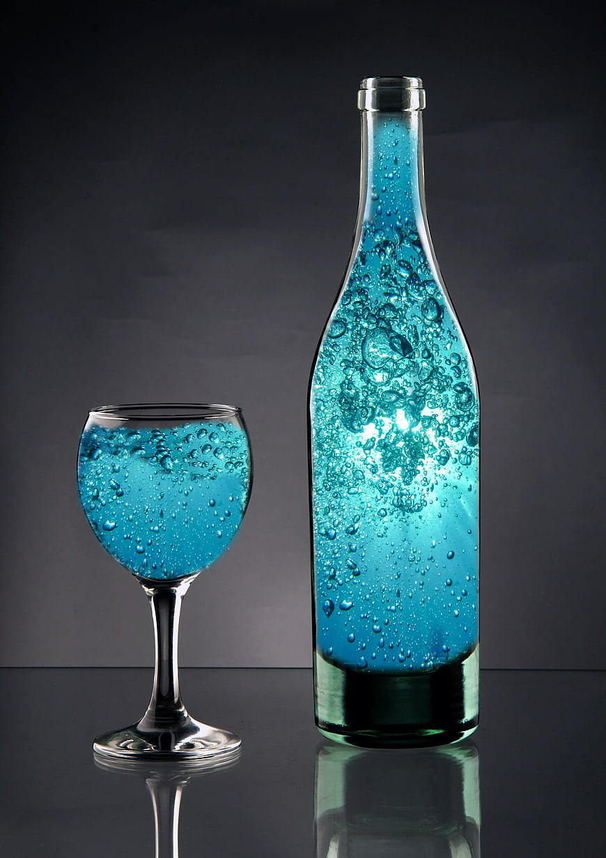 Blue Sparkling Liquid in Glass Bottle and Wine Glass