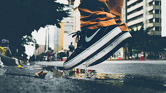 Low angle shot of black sneakers splashing in a puddle