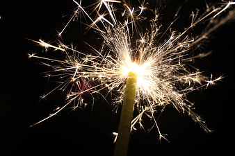 Close-up of a burning sparkler with bright sparks against a black background