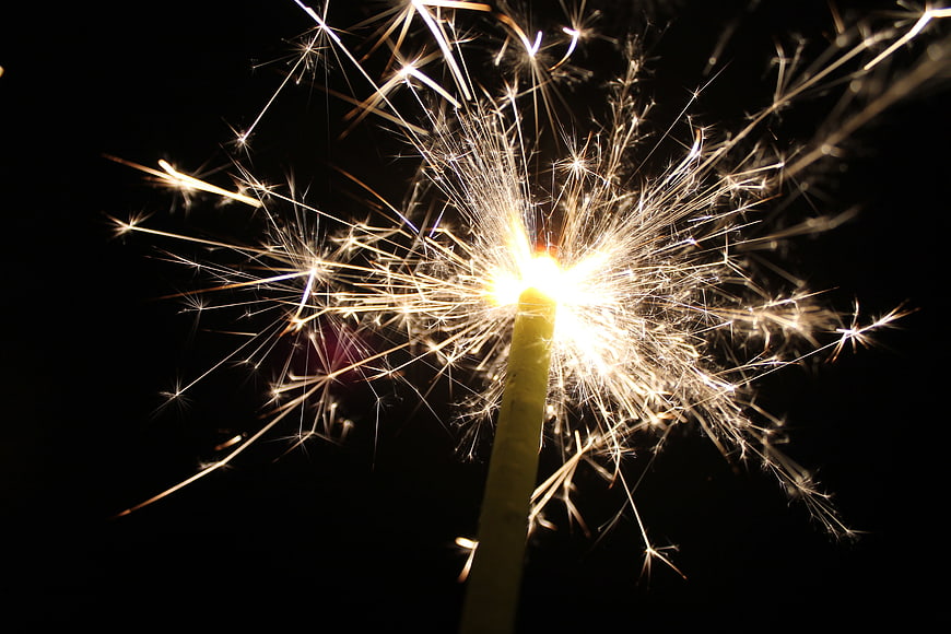 Close-up of a burning sparkler with bright sparks against a black background