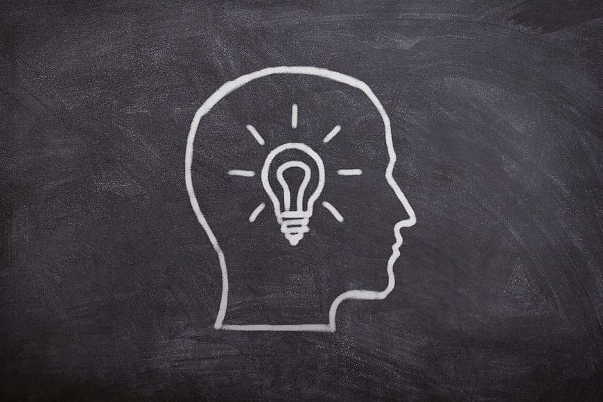 Chalk drawing of human head profile with lightbulb idea symbol on blackboard