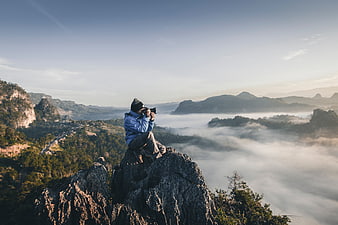 Photographer capturing misty mountain landscape from rocky summit