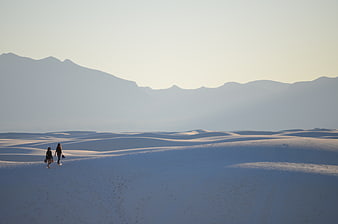 Two women walking on white sand dunes with mountains
