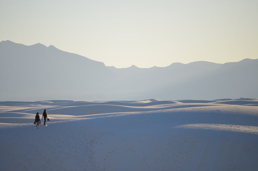Two women walking on white sand dunes with mountains