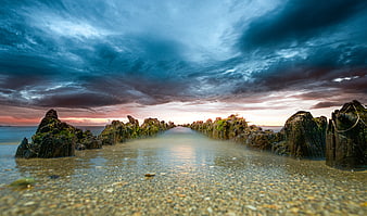 Dramatic Sunset Over Mossy Wooden Breakwater on Pebble Beach