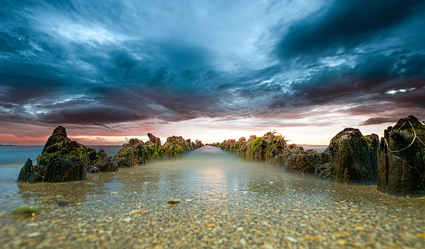 Dramatic Sunset Over Mossy Wooden Breakwater on Pebble Beach