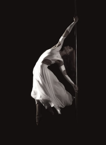 Dramatic Pole Dance Performance in White Dress Against Black Background