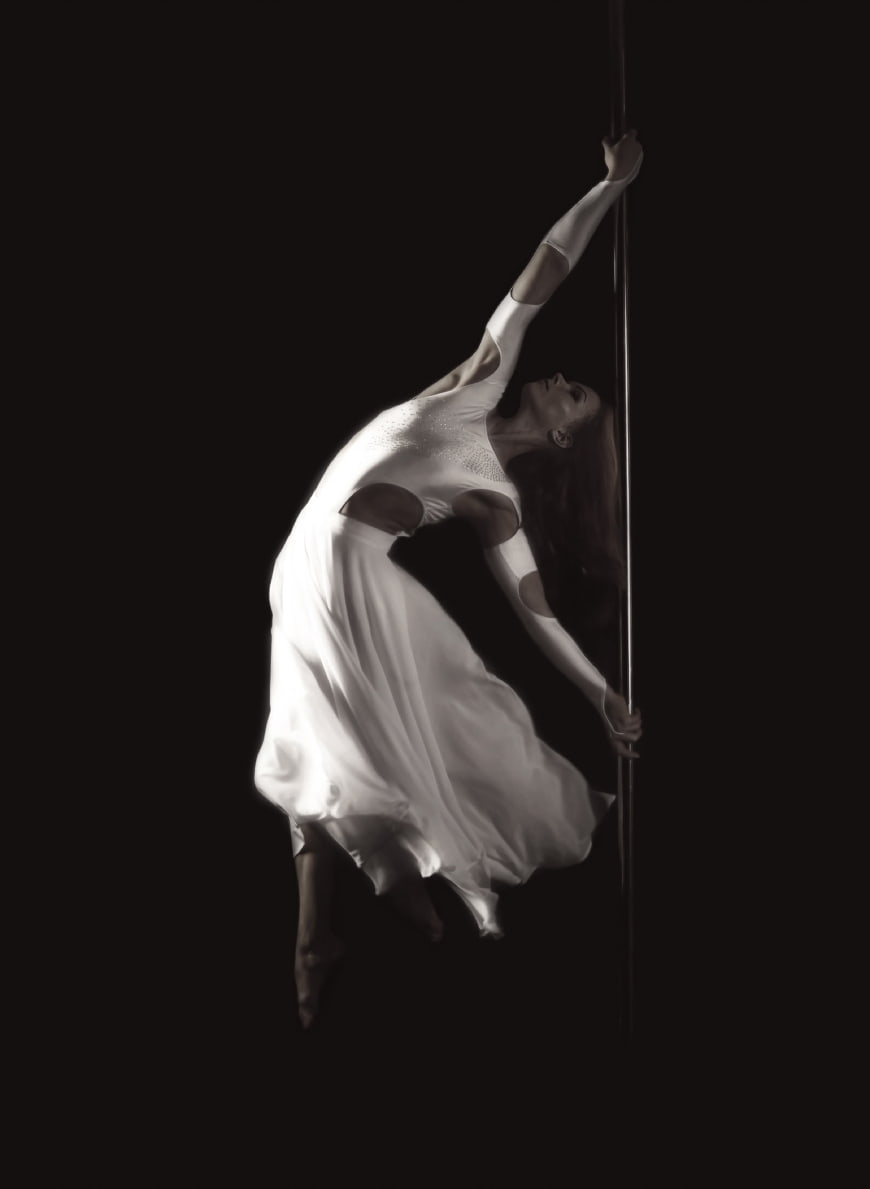 Dramatic Pole Dance Performance in White Dress Against Black Background
