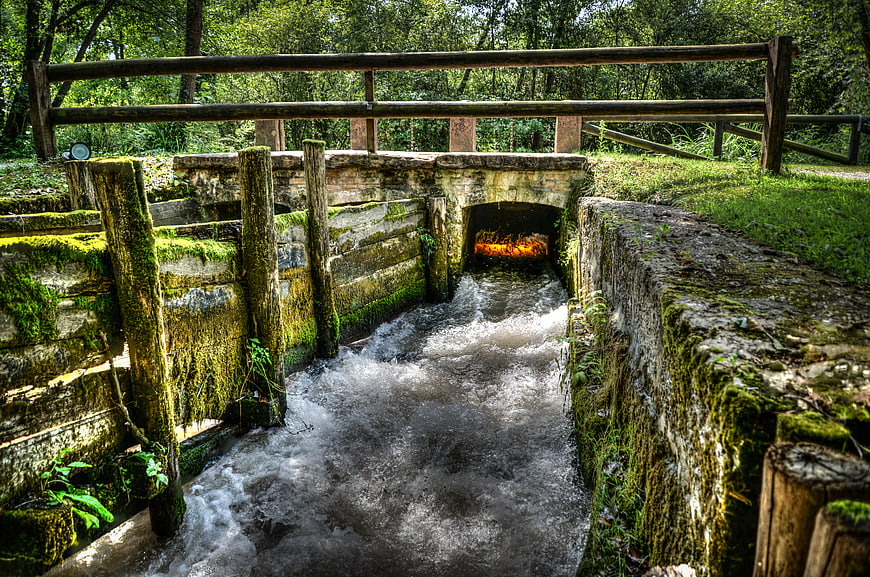 Rushing water flowing through mossy stone sluice gate in forest