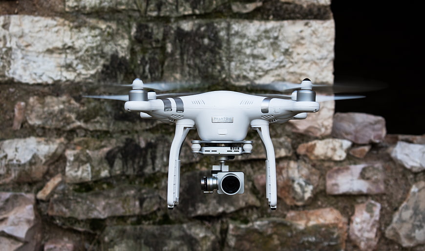 White drone hovering in front of stone wall