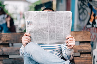 Man reading newspaper on wooden bench in urban setting