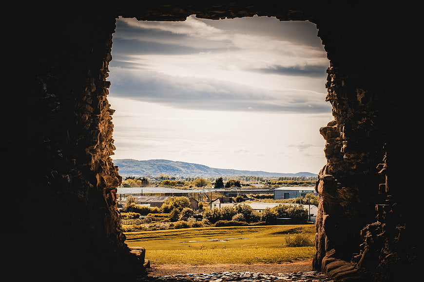 Rustic stone window frame overlooking green farmland and mountains