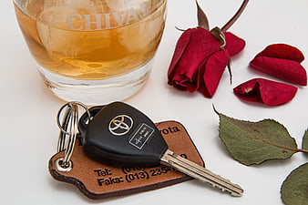 Whiskey glass and car keys with red rose on white background