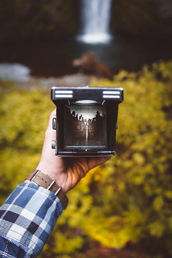 Hand holding vintage medium format camera with waterfall background