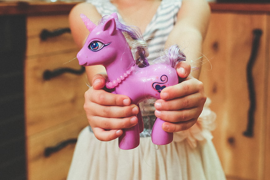 Child Holding Purple Plastic Unicorn Toy