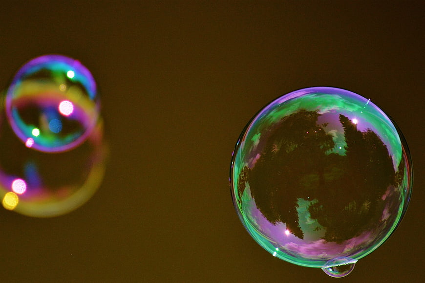 Iridescent soap bubbles reflecting trees against dark background