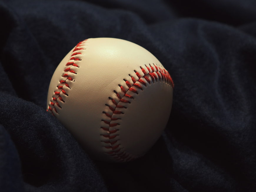 Close-up of a baseball with red stitching on dark fabric