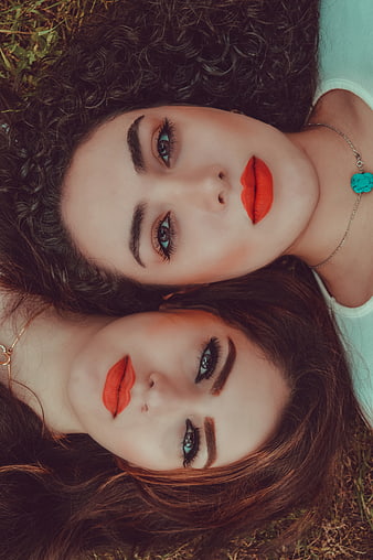 Close-up portrait of two women with red lipstick lying on grass