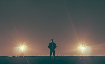 Silhouette of Man Standing Between Two Bright Lights at Sunset
