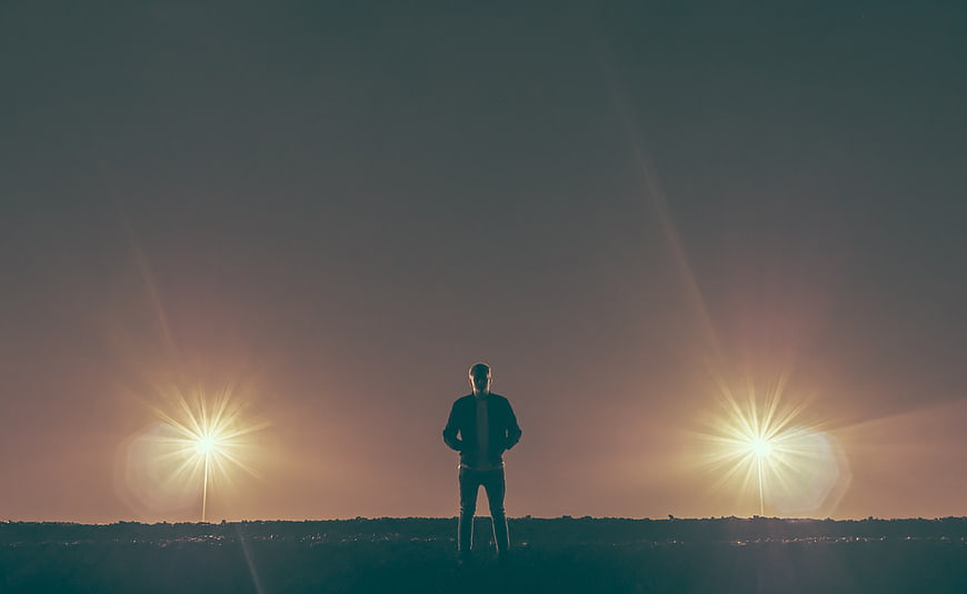 Silhouette of Man Standing Between Two Bright Lights at Sunset