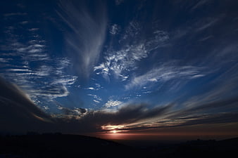 Dramatic sunset with sweeping clouds over dark silhouette landscape