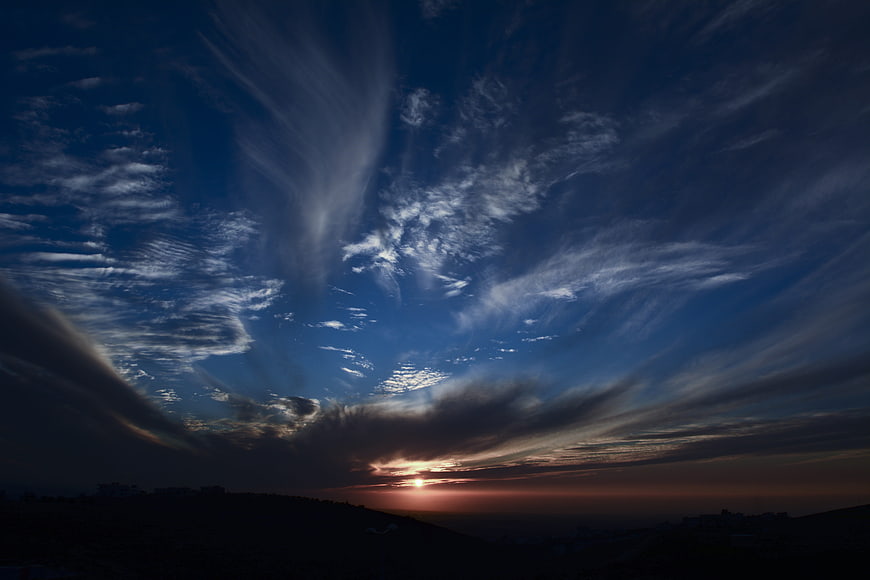 Dramatic sunset with sweeping clouds over dark silhouette landscape
