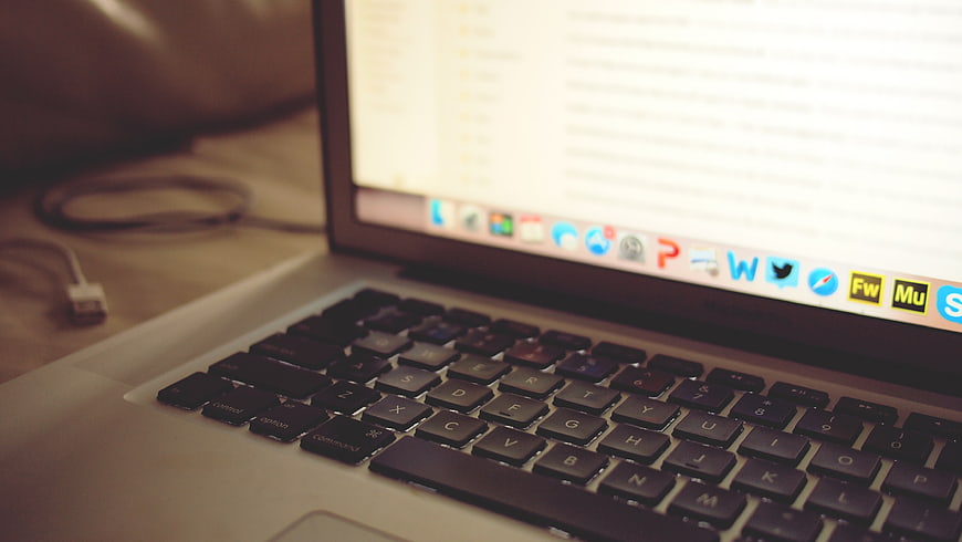 Close-up of MacBook keyboard with blurred screen and dock icons