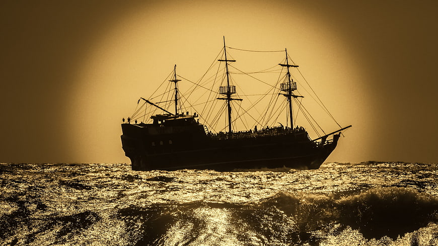 Silhouette of a Three-Masted Sailboat on Golden Ocean Waves