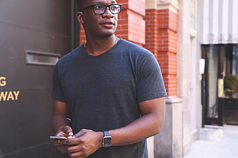 Young Black Man with Glasses Holding Smartphone Outdoors