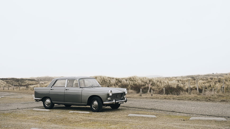 Vintage gray classic car parked on gravel road near dunes