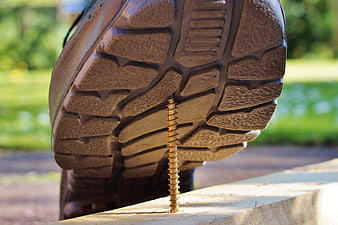 Close-up of work boot sole stepping on a sharp screw