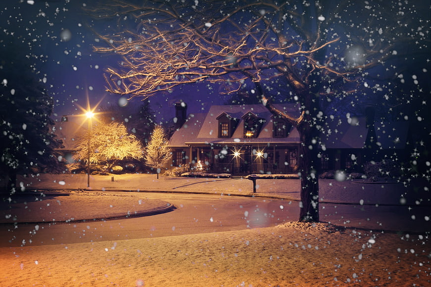 Snowy suburban house at night with falling snow and streetlights