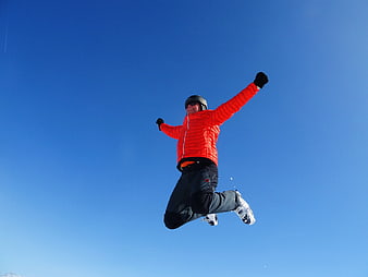 Man in red jacket jumping in the air against a clear blue sky