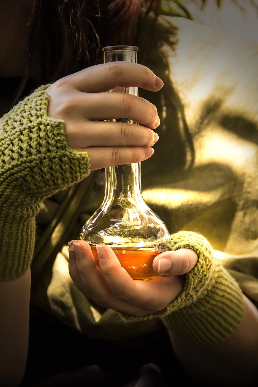 Hands holding glass flask with amber liquid in cozy green sweater