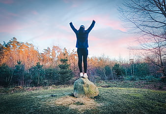 Woman standing on rock with arms raised in nature