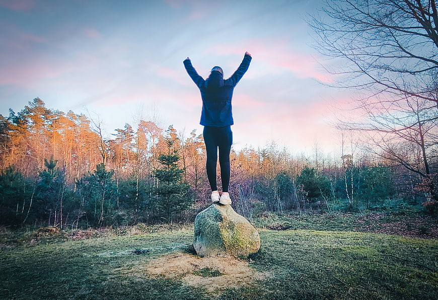 Woman standing on rock with arms raised in nature