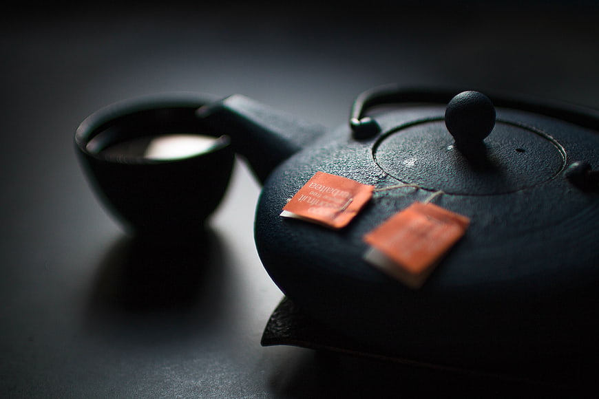 Dark Teapot and Cup with Tea Bags on Black Surface