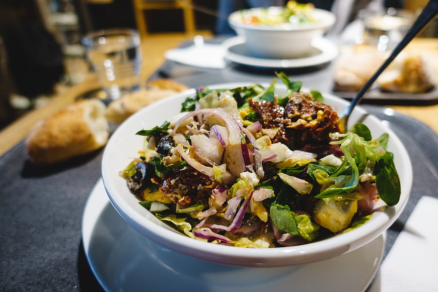 Fresh mixed salad with red onions and dressing in a white bowl