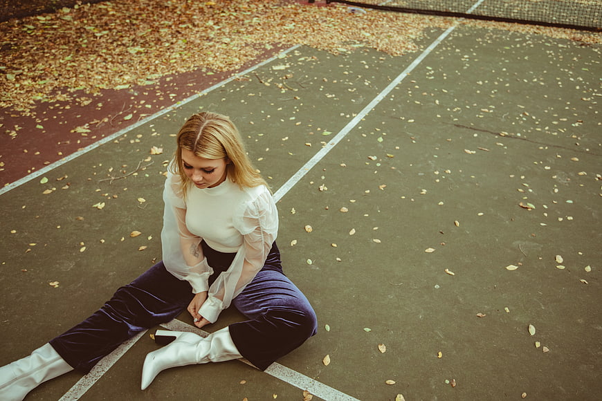 Blonde Woman in White Boots Sitting on Tennis Court in Autumn